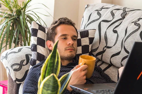 happy and attractive man having a coffee and consulting his laptop at home