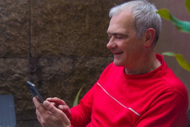 Olgun bir adam cep telefonu kullanarak terasta oturuyor.