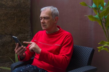 Olgun bir adam cep telefonu kullanarak terasta oturuyor.