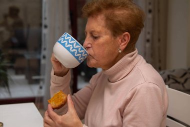 Kahvaltıda kahve içip tost yiyen son sınıf öğrencisi kadın.