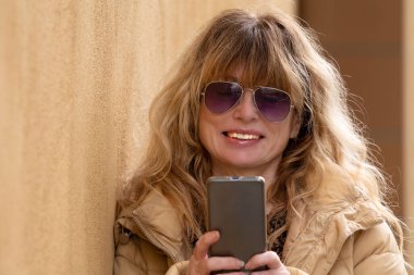 Sarı duvarda akıllı telefonu olan gülümseyen kadın filtresiz.