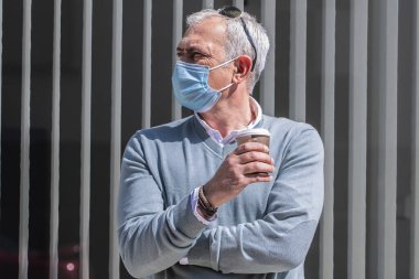 Tıbbi maskeli yetişkin bir adam şehirde yemek alıyor.