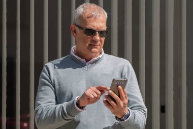 Yetişkin bir adam sokakta onun cep telefonunu arıyor ve kontrol ediyor.