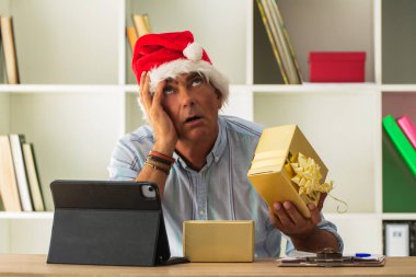 Noel Baba şapkalı ve stresli bir adam. Ofiste ya da evde noel hediyelerini açıyor.
