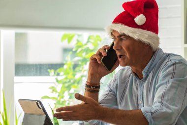 Noel Baba şapkalı ve cep telefonlu bir adam.