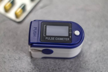 Nabız oksimetresi ve açık gri arkaplanda haplar.