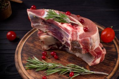 Kemiğin üzerinde birkaç parça çiğ et, kızılcık, biberiye ve ahşap arka planda kiraz domatesli.