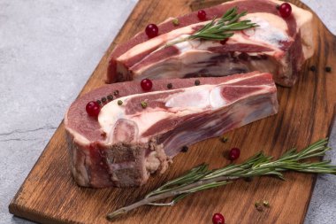 Kemiğin üzerinde taze çiğ et parçaları ve ahşap bir tahtada kızılcık ve biberiye var.