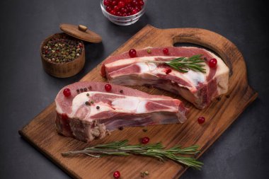 Koyu bir zemin üzerinde, üzerinde kızılcık, biberiye ve baharat bulunan taze sığır eti parçaları..