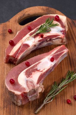 Kemiğin üzerinde taze çiğ et parçaları ve ahşap bir tahtada kızılcık ve biberiye var.