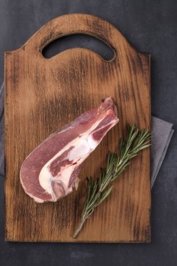 Koyu arkaplanda tahta bir tahtanın kemiğinde taze çiğ et parçası var..