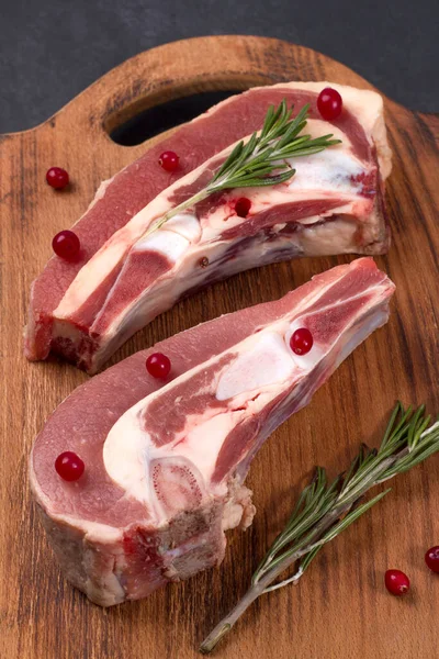 Kemiğin üzerinde taze çiğ et parçaları ve ahşap bir tahtada kızılcık ve biberiye var.