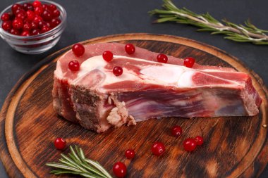 Kemiğin üzerinde taze çiğ et parçaları ve ahşap bir tahtada kızılcık ve biberiye var.