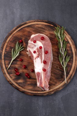 Kemiğin üzerinde taze çiğ et parçaları ve ahşap bir tahtada kızılcık ve biberiye var.