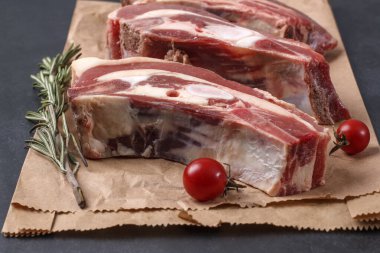 Kemiğin üzerinde taze çiğ et parçaları, kiraz domatesleri ve ambalaj kağıdında biberiye.