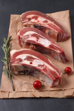 Kemiğin üzerinde taze çiğ et parçaları, kiraz domatesleri ve ambalaj kağıdında biberiye.