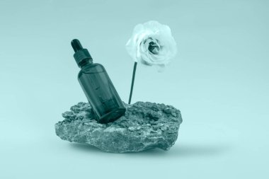 Kehribar cam şişe taş bir kaide üzerinde kozmetik için. Tiderwater Yeşili renginde bir östoma çiçeği. 2022 'nin moda rengi..