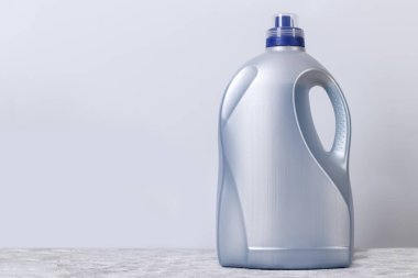 Gray large plastic bottle for liquid laundry detergent against the wall with copy space.