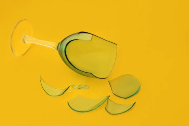 Sarı zemin üzerinde cam parçaları olan kırık cam şarap kadehi..