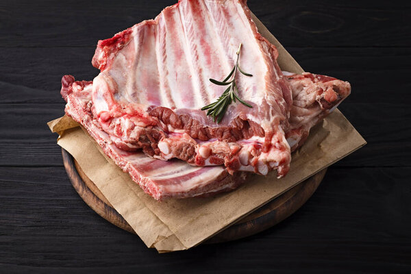 Raw pork ribs on a wooden board on a dark background.