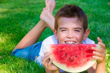 Çimlerin üzerinde bir dilim karpuz olan çocuk.