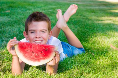 Çimenlerde karpuz yiyen tatlı çocuk.
