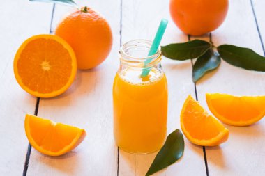 Bardakta taze portakal suyu ve ahşap arka planda bir sürahi portakal.