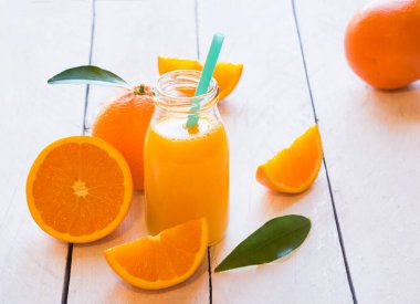 Bardakta portakal suyu ve beyaz ahşap arka planda taze portakallar