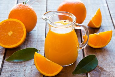 Bardakta portakal suyu ve ahşap arka planda taze portakallar.