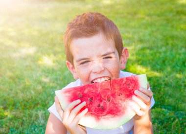 Parkta karpuz yiyen genç bir çocuk.