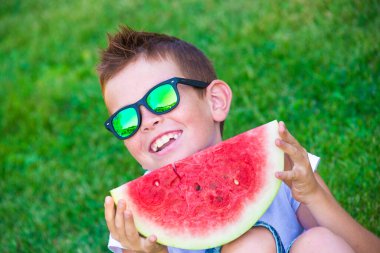 Çimlerde karpuz taşıyan genç bir çocuk.