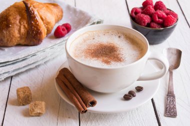 Bir fincan kruvasan ve ahşap arka planda taze böğürtlenli kahve.