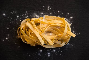 Siyah zemin üzerinde un olan çiğ makarna.