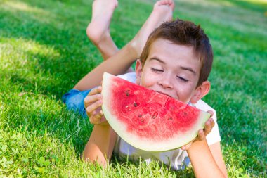 Parkta karpuz yiyen genç bir çocuk.
