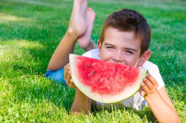 Parkta karpuz yiyen genç bir çocuk.