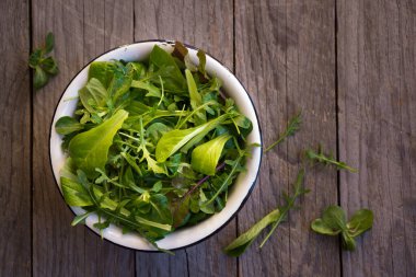 Taze sebze salatası roka ve diğer yapraklar koyu ahşap bir kasede.