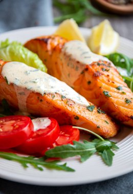 Pişmiş somon balığı fileto, otlar, limon ve sebzeler.