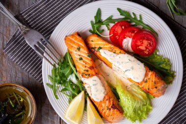 Pişmiş somon balığı fileto, otlar, limon ve sebzeler.