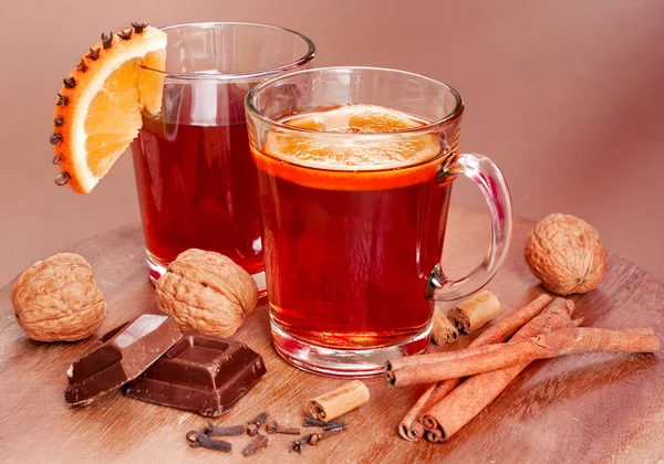 cup of hot tea with cinnamon sticks, chocolate and nuts on wooden background