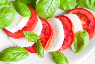 Beyaz tabakta mozzarella, fesleğen ve domates salatası.