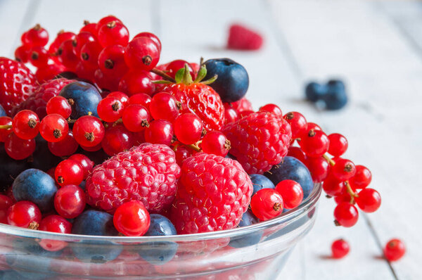 fresh ripe berries in glass bowl on wooden table