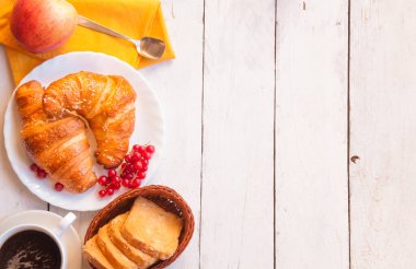 Kahvaltıda kruvasan, bir fincan kahve ve ahşap masada kruvasan.