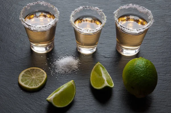 tequila glasses with lime and salt on wooden background