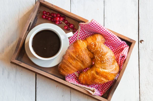 breakfast with croissants, cup of coffee and berries on wooden table