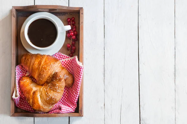 breakfast with croissants, cup of coffee and berries on wooden table