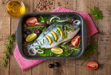 Ahşap zemin üzerinde sebze ve baharatlı çiğ dorado balığı.