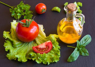 Siyah arka planda zeytinyağı, domates, marul ve fesleğen.