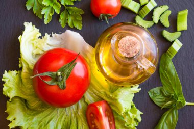 Siyah arka planda zeytinyağı, domates, marul ve fesleğen.