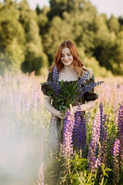 Lupin çalılığında kızıl saçlı bir kızın portresi..