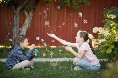 Erkek ve kız kardeş bahçede sabun köpüğü üflüyorlar..
